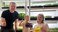 Family display a tray of vibrant microgreens inside a facility filled with thriving plants, giving a thumbs up.