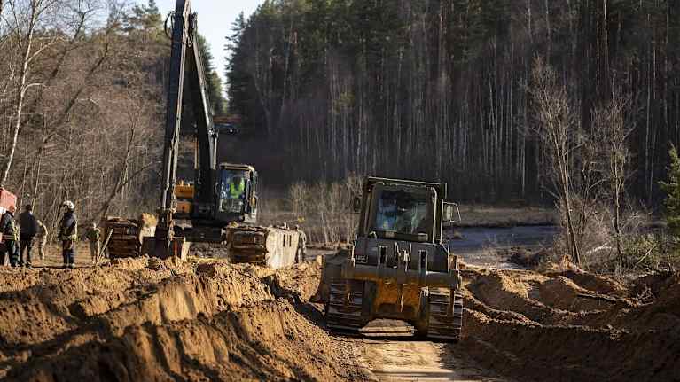 Kaksi kaivinkonetta tasaa ja kaivaa maata suo laidalla. kaivinkonetta.