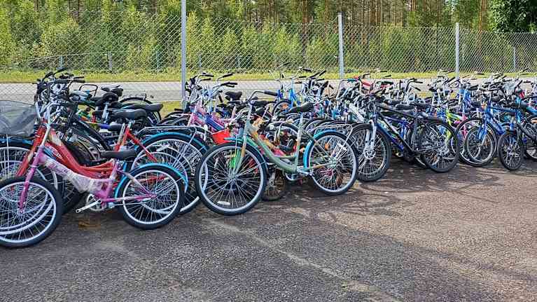 Kymmeniä erivärisiä ja erikokoisia polkupyöriä nojallaan metalliaitaa vasten.
