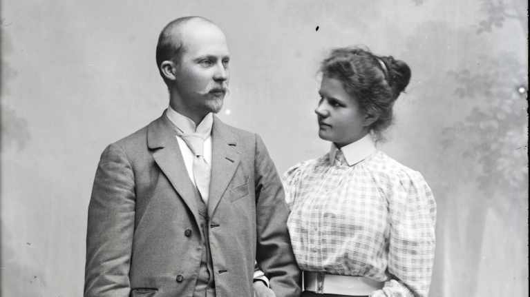 Mustavalkoisessa valokuvassa kihlaparin näköinen nuori pariskunta vuosisadan vaihteesta.  