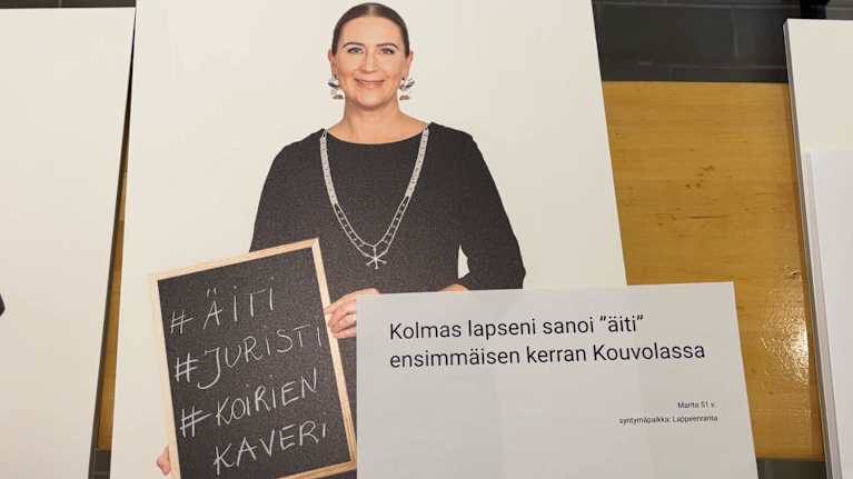 Nainen pitelee taulua, jossa lukee äiti, juristi ja koirien kaveri.