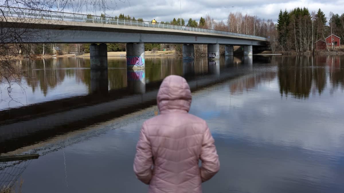 Tyttö vaaleanpunaisessa takissa seisoo joen rannalla. Kuva on anonyymi.