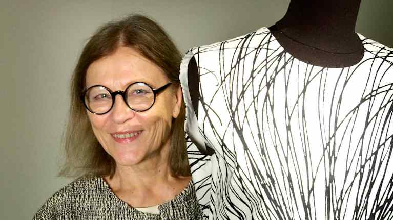 A smiling woman stands next to a mannequin.