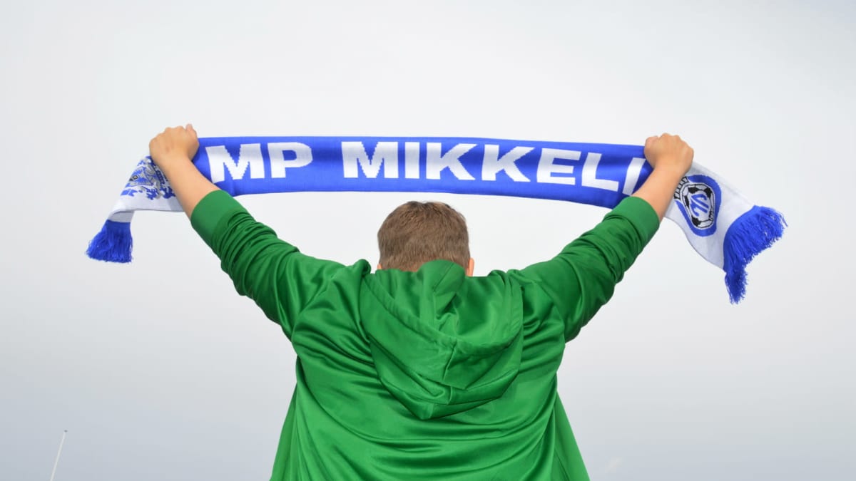 Mies pitää korkealla käsiensä välissä fanihuivia, jossa lukee MP Mikkeli.