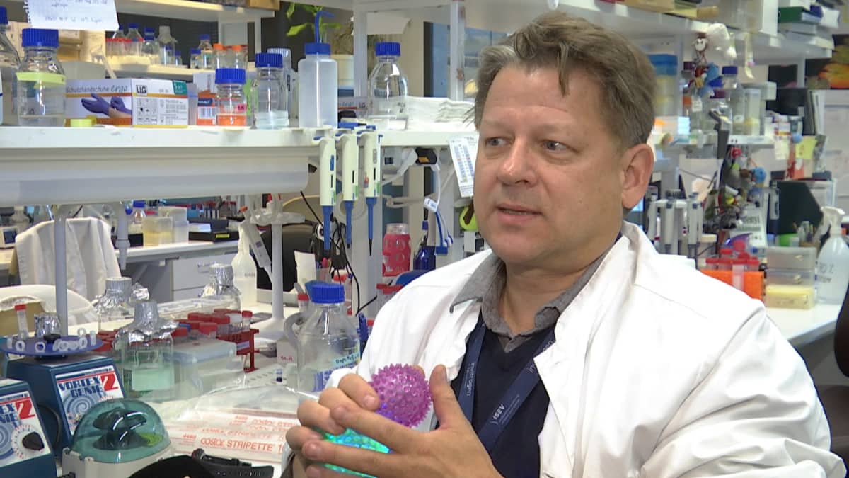 Valkotakkinen keski-ikäinen mies laboratoriolaitteiden ympäröimänä. 