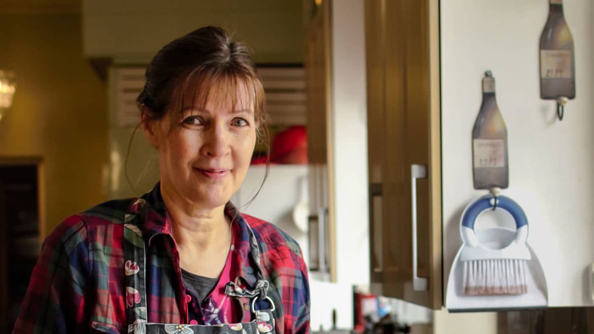 Liisa Mankinen seisoo keittiössä ruoanlaittovälineitä kädessään.