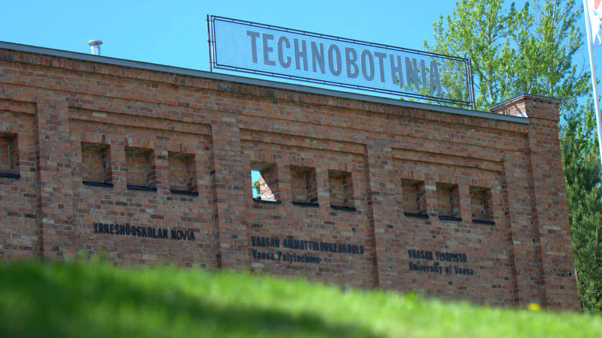 Etualalla nurmikkoa, taustalla Technobotnian tiiliseinä ja kyltti.