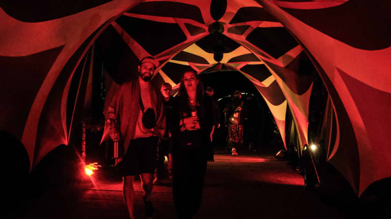 Ihmisiä kävelee värivaloin valaistussa kankaisessa tunnelissa Kosmos Festivalilla.