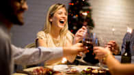 En kvinna skrattar och skålar vid ett julbord med sina vänner.