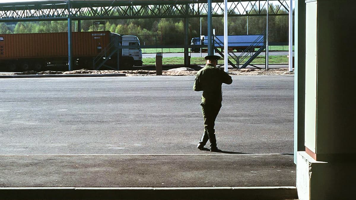 Rajamies seisoo raja-asemalla selkä kameraan päin. Taustalla rekka-auto. 