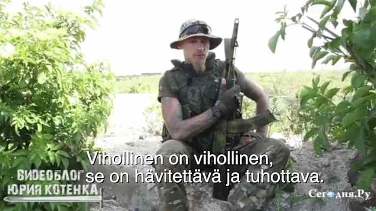 Petrovski istuu kivellä tai vastaavalla, ase sylissä, sotilasvaatteissa. Kuva on ruutukaappaus televisiolähetyksestä. Päällä on suomenkielinen tekstitys: "Vihollinen on vihollinen, se on hävitettävä ja tuhottava." 