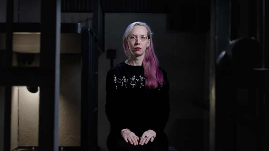 Detransitioitunut nainen "Sametti" katselee seinälle heijastettua valokuvaansa naisena.