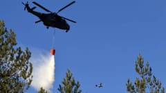 Helikopteri sammuttaa maastopaloa. Taustalla tähystyskone.
