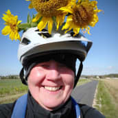 Rauni Hietanen poseeraa lähikuvassa auringonkukkia pyöräilykypärässään.