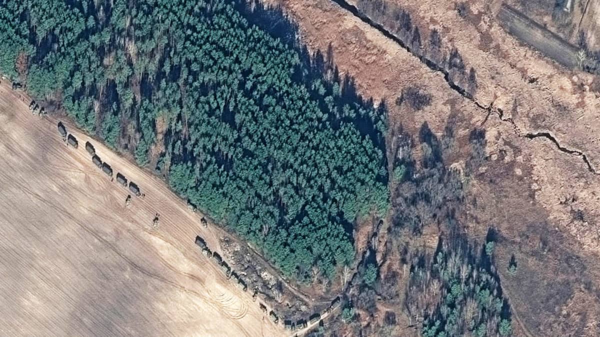 Satelliittikuva metsästä ja pellosta, jonka reunaa etenee sotilasajoneuvosaattue. 