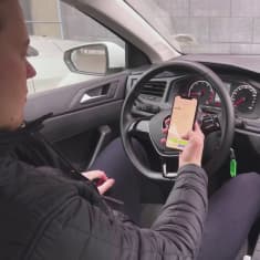 Mies ottaa yhteiskäyttöautoa käyttöön puhelinsovelluksella, autossa istuen.