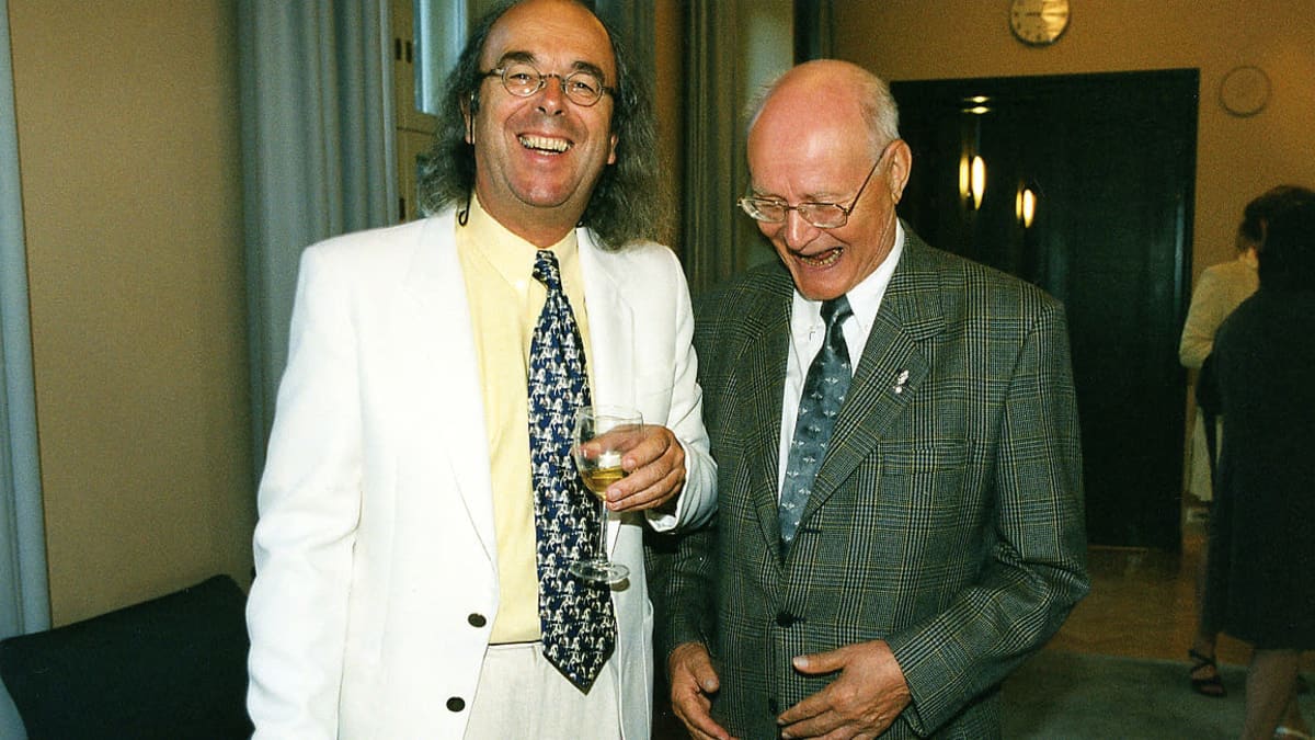 Urkusoitintaiteilija Guy Bovet ja Lahden Urkuviikon johtaja Aimo Känkänen kaupungin vastaanotolla vuonna 2001. Bovetilla valkoinen puku päällään, molemmat nauravat, Bovet katsoo kameraan, Känkänen hieman kumarassa katsoo alaspäin ja nauraa.