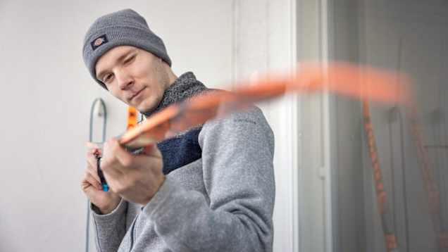 Kuvassa hiihtäjä pitelee suksea kädessä ja katselee sen pohjaa toinen silmä kiinni.