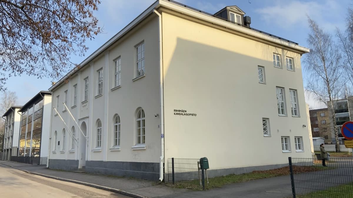 Vaaleankeltainen kaksikerroksinen Riihimäen kansalaisopiston rakennus kadun varressa syysauringossa.