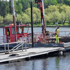 Satama 1 -niminen työlautta on ajanut mattolaiturin kupeeseen kylki laituria kohti. Kannella on huomioväriisiin vaatteisiin pukeutunut työntekijä.