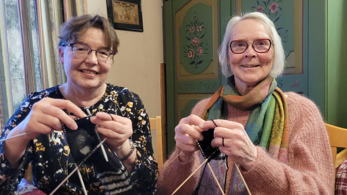 Kaksi naista istuu keittiössä kutomassa villasukkia lahjoitettavaksi Ukrainaan