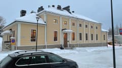 Keltainen hirsirakennus lumisen kadun varrella. 