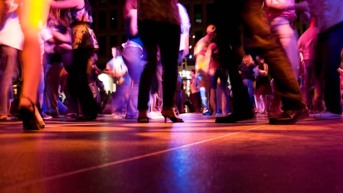 nerifrån syns golvet och en massa skor och kläder från där folk dansar på ett dansgolv i mörkt ljus