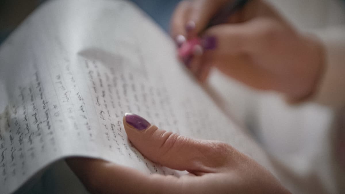 Lähikuvassa kädet, jotka pitelevät paperilla, jolla on käsinkirjoitettua tekstiä.