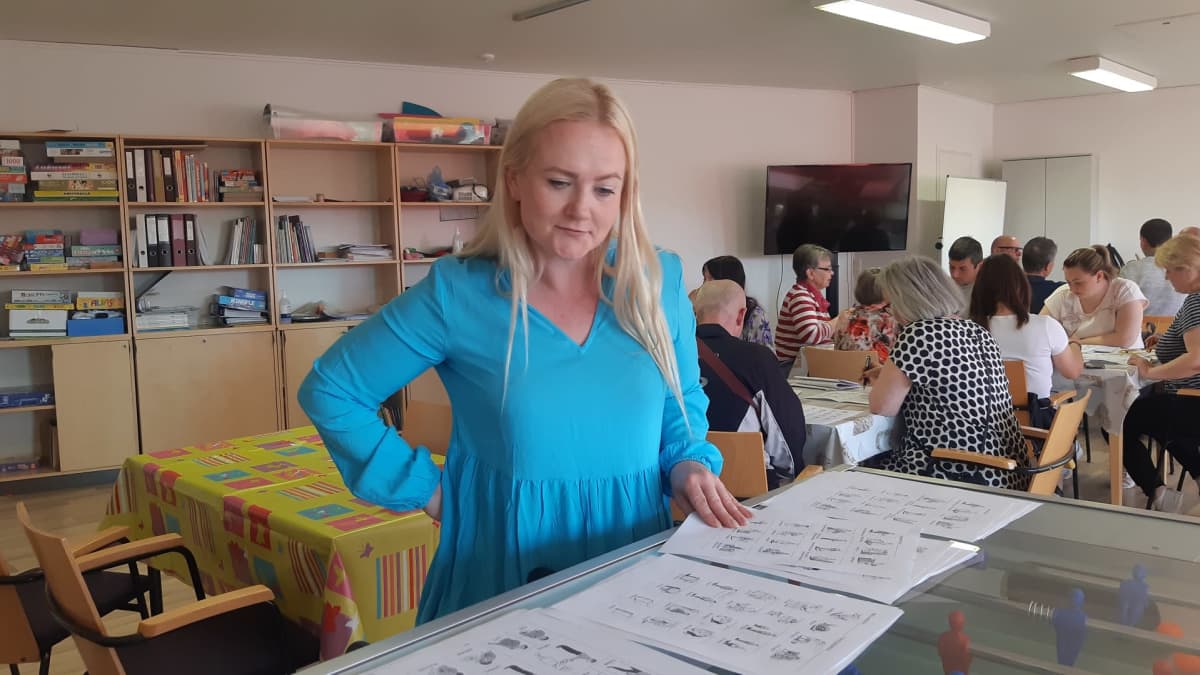 Monikulttuurisen työn ohjaaja Riikka Rajala katselee papereita, joissa esitellään suomen kielen sanoja piirrosten avulla. Taustalla ukrainalaispakolaisia opettajineen opiskelemassa.