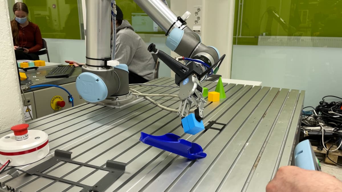 Robottikäsi siirtää palikkaa.