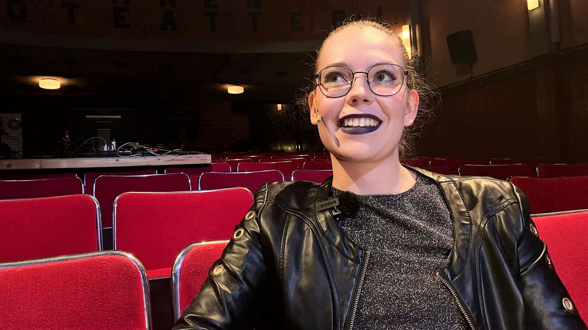 Silmälasipäinen nuori nainen hymyille teattertin katsomossa.