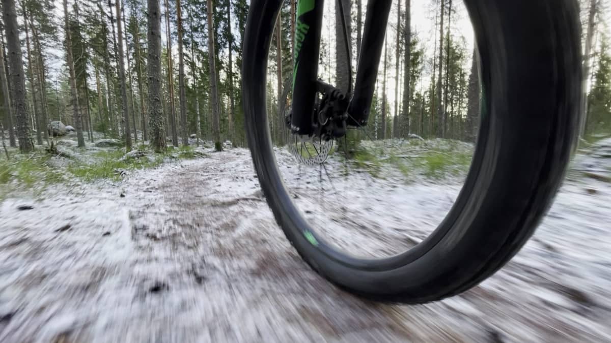 Maastopyörän eturengas kiitää hivenen lumisella metsäpolulla.