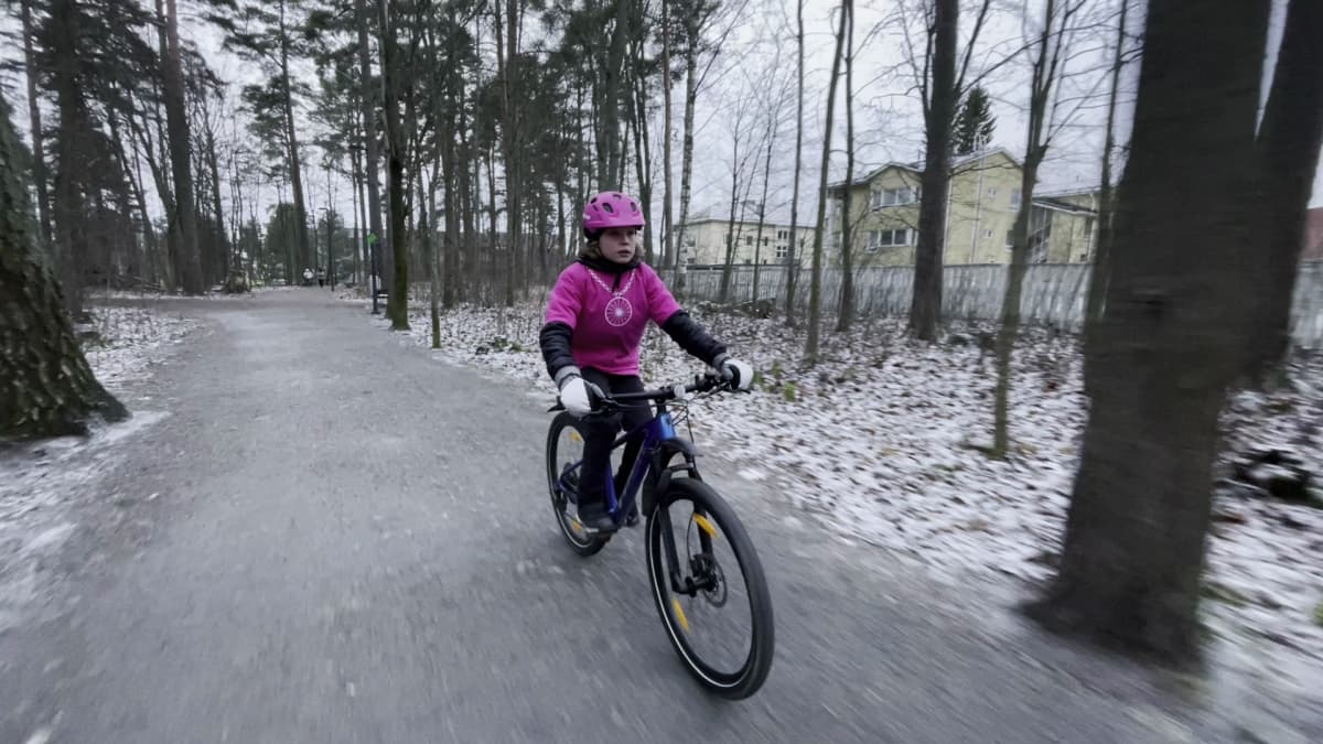 Lapsipyöräilypormestari Pinja Vienola pyöräilee hiekkatiellä pienessä hivenen lumisessa metsässä.