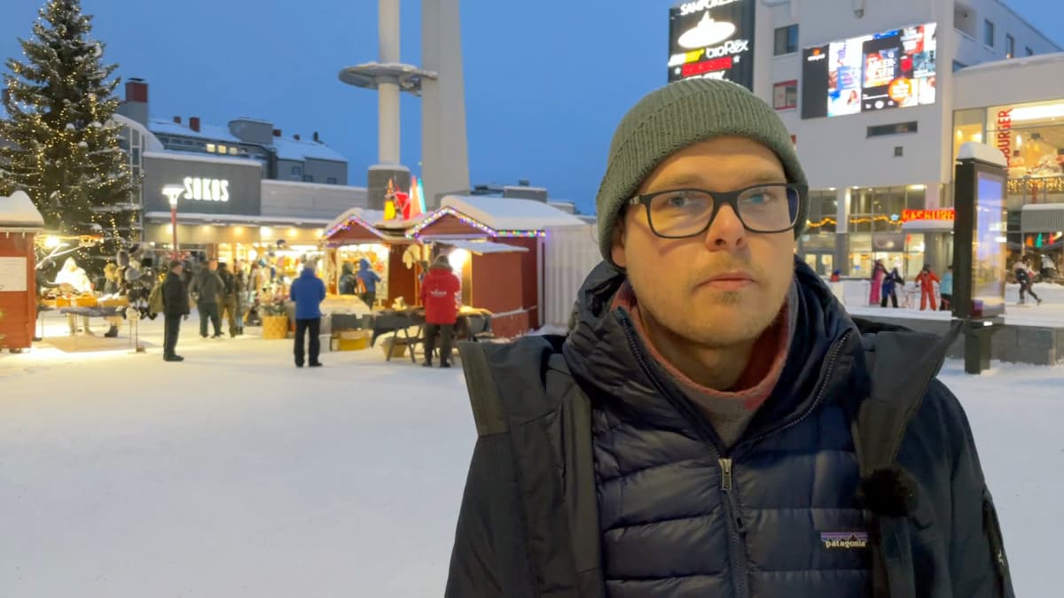 Valotaiteilija Jukka Huitila seisoo Rovaniemen ydinkeskustassa mainosvalojen ympäröimänä.