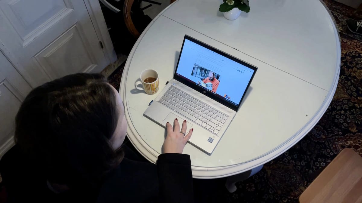 Tummahiuksinen nainen selaa uutisjuttua kannettavalla tietokoneellaan. 