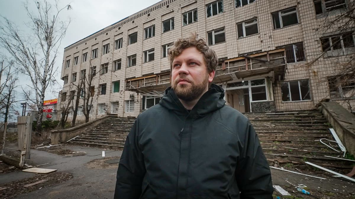 Sellisti Lukas Stasevskij katsoo ohi kameran, taustalla tuhottu rakennus.