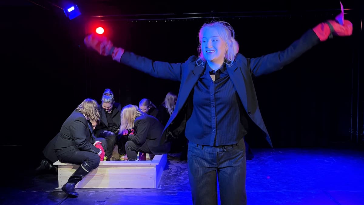 Nainen nostaa kädet ilmaan voittajan elkein teatterin näyttämöllä.