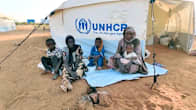 Kaksi naista ja kolme lasta istuvat UNHCR:n teltan edessä Sudanissa.