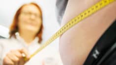 A woman measures a man's waist using a measuring tape.