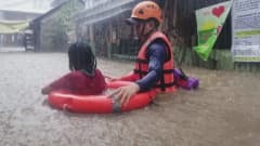 Pelastustyöntekijä auttaa naista tulvan keskellä Filippiineillä.