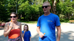 Nainen punaisessa topissa, mies sinisessä t-paidassa ja tyttö sinisessä t-paidassa seisovat puistossa.