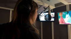 Anna Näkkäläjärvi-Länsman studiossa dubbaamassa Viljonkalle ääniä. Hänen edessä on mikrofooni ja taustalla näkyy ohjelma.