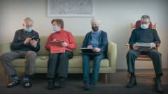 Neljä ikäihmistä istuu sohvalla tabletit käsissään ja maskit kasvoillaan. Yksi heistä näyttää älypuhelimesta toiselle jotakin.