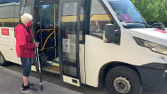 Vanhempi nainen kävelykeppien kanssa on nousemassa minibussiin.