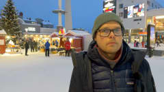 Valotaiteilija Jukka Huitila seisoo Rovaniemen ydinkeskustassa mainosvalojen ympäröimänä.