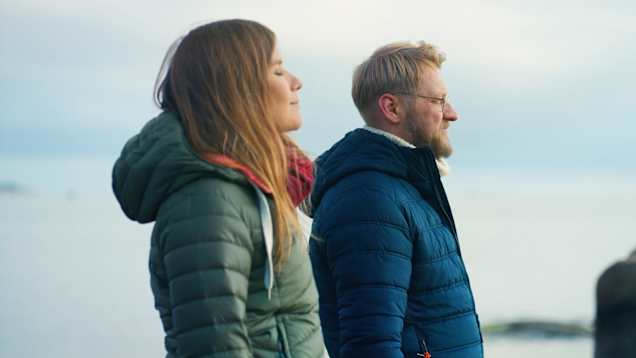 Kaksi henkilöä lämpimissä takeissa merenrannalla.