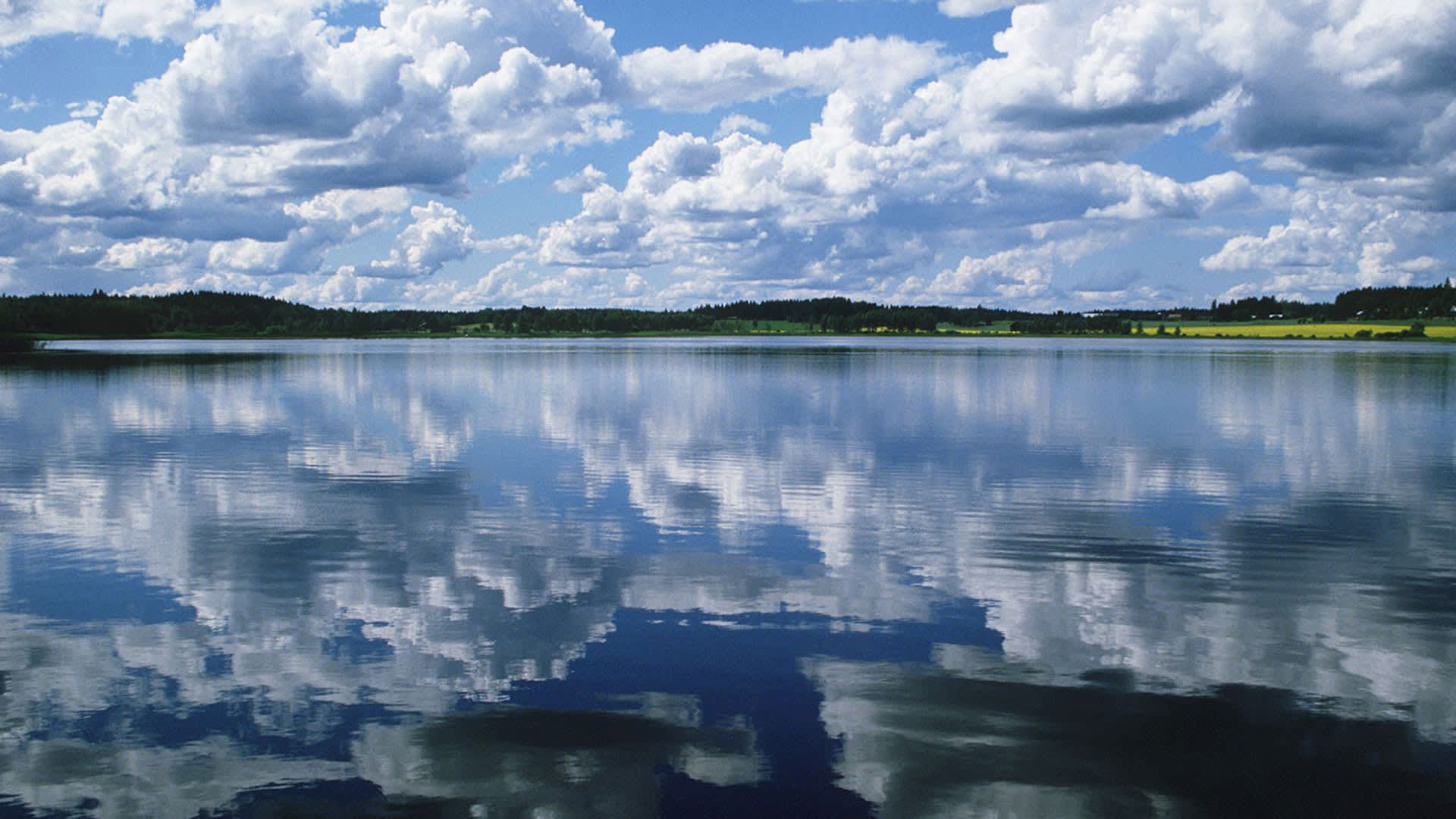 Pilvet kuvastuvat tyyneen järven pintaan.