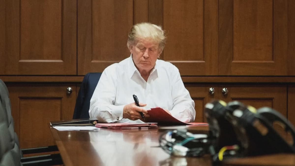 Donald Trump istuu pöydän ääressä sairaalassa ja katsoo papereitaan