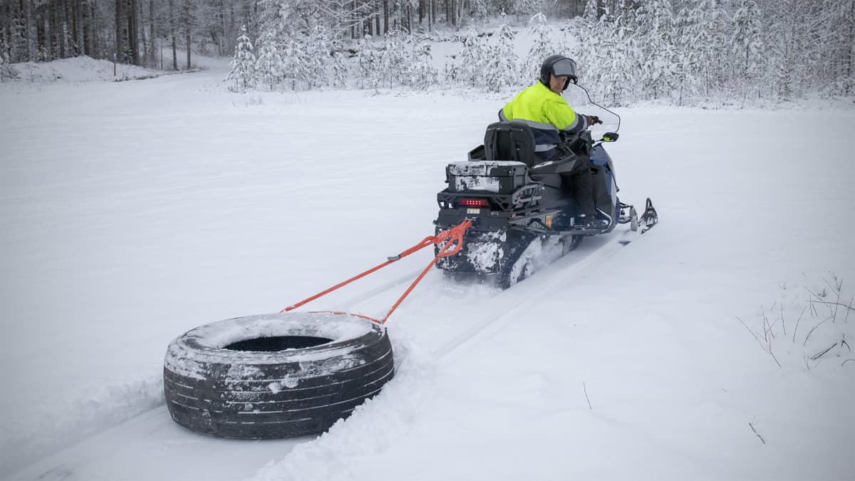 Harry Jussila vetään moottorikelkalla rengasta, joka avaa kävelijöille uraa lumeen.