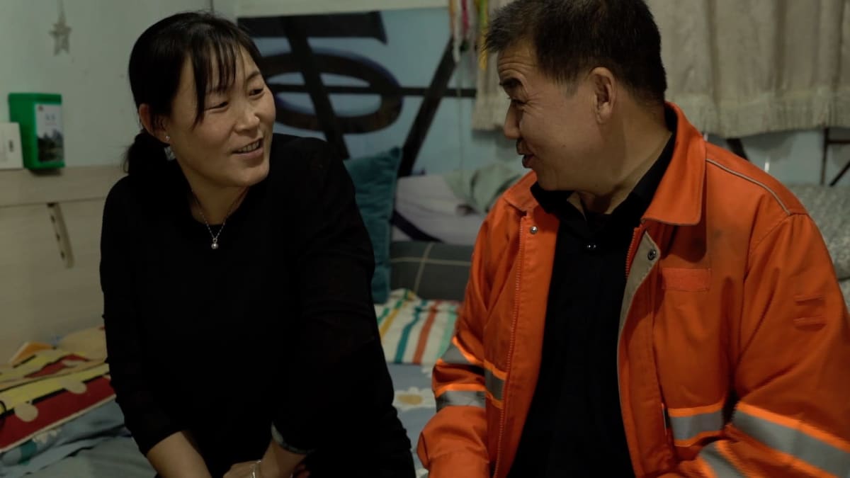 kiinalainen keski-ikäinen pariskunta istuu sängyn päällä ja juttelee
